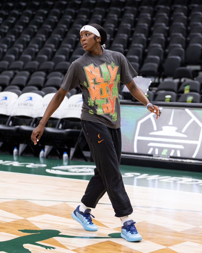 A player on a basketball court wears a gray t-shirt that reads "play with joy" and a white headband.