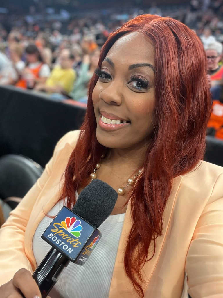 Terrika Foster-Brasby holds a NBC Sports Boston microphone while wearing an orange blazer.