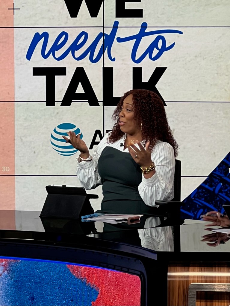 Terrika Foster-Brasby sits at a desk holding her hands up as she makes a point.