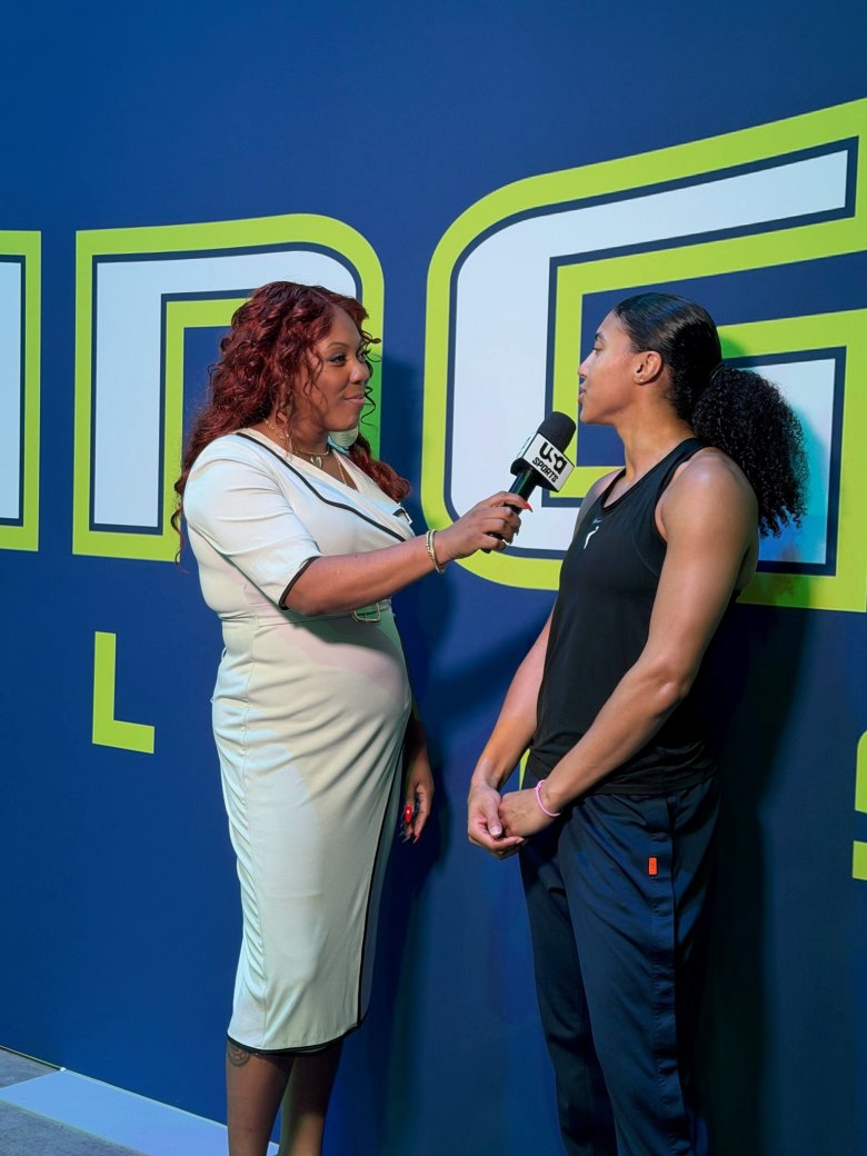 Terrika Foster-Brasby holds a mircophone while wearing a white dress as she interviews Azzi Fudd, who is wearing a black tank top and navy sweatpants.