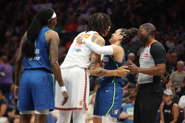 Brittney Griner in her white uniform leans over to hug Kayla McBride, who's wearing blue