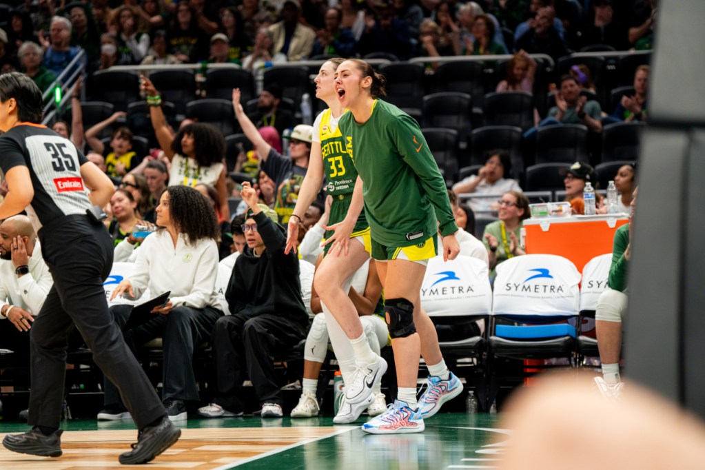Mackenzie Holmes stands and yells in celebration next to the bench.