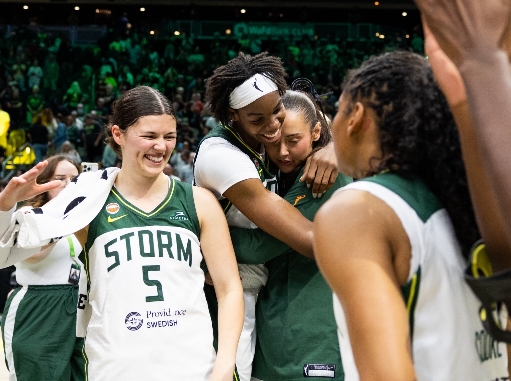 In the center of the photo, Dominique Malonga and Mackenzie Holmes engage in a tight embrace while Jade Melbourne in the foreground goes to dap up <a rel=
