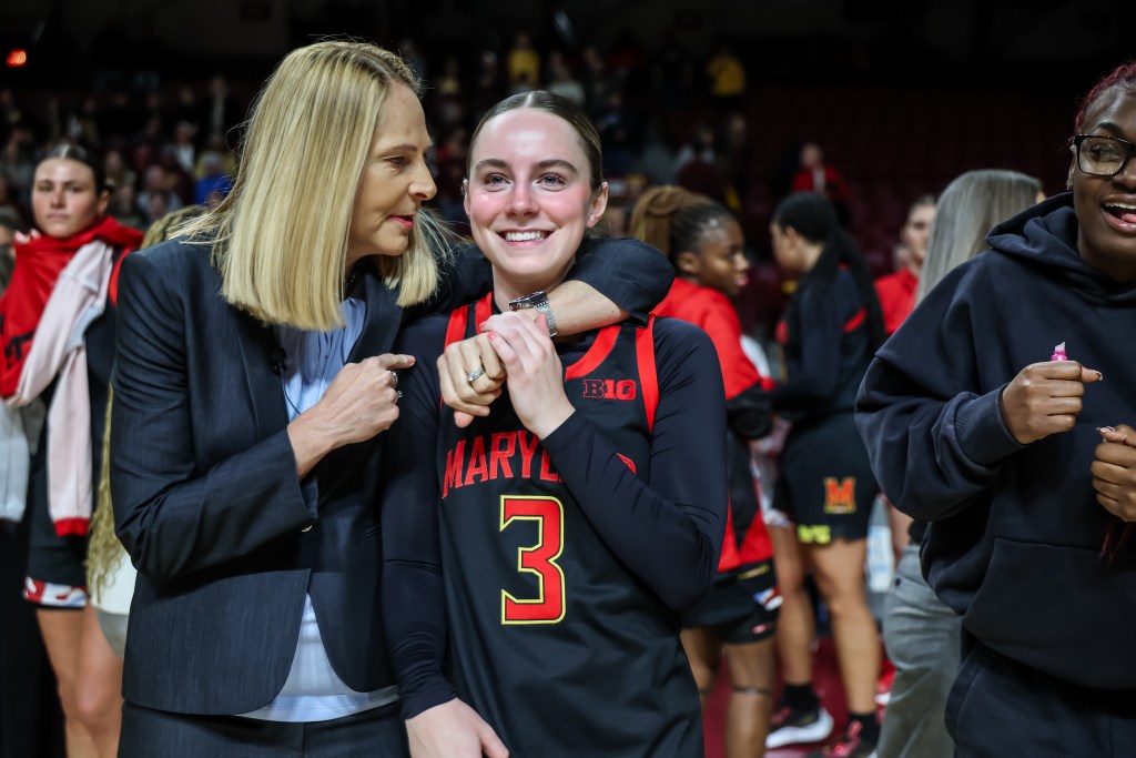 Addi Mack wearing a black jersey is smiling and being hugged by head coach Brenda Frese.