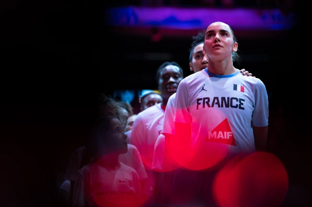 Basketball players in France warmup shirts line up on the basketball court before a game, with children next to them