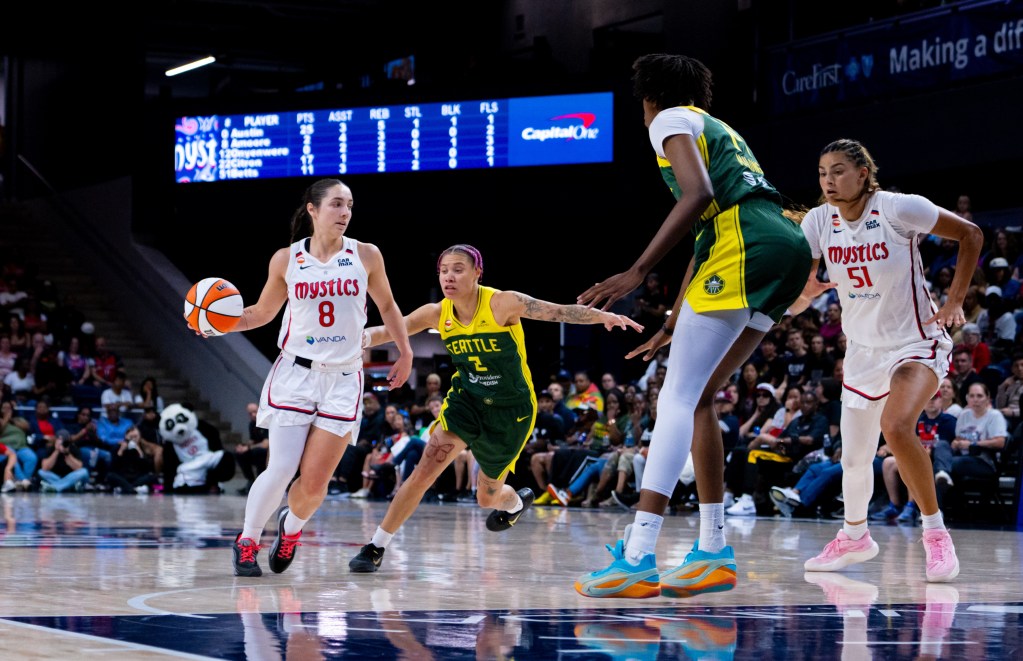 Washington Mystics point guard Georgia Amoore dribbles the ball with her right hand near the top of the key. Her defender is a step behind her, and a help defender is at the free throw line. Mystics center Lauren Betts is turning to run into the lane.