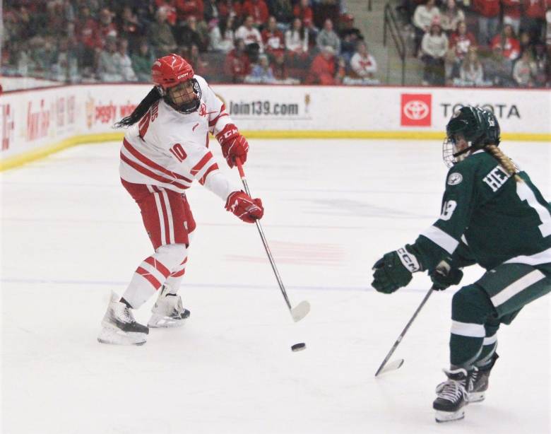 A women's hockey player shoots the puck while another player defends.