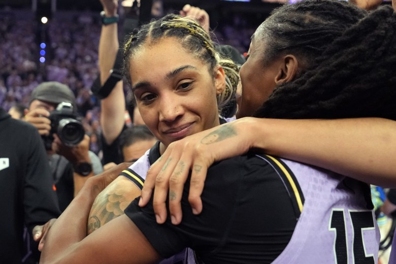 Golden State Valkyries forward Gabby Williams and Tiffany Hayes hug after winning a playoff game. They are shown up close, from about chest height up. In the background, photographers take their photo from other angles.