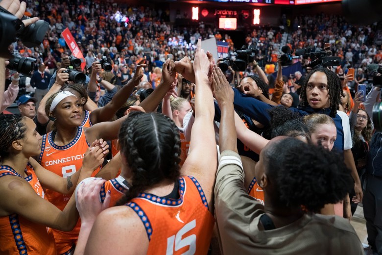 The Connecticut Sun huddle in a circle with all their hands up in the air at the center.