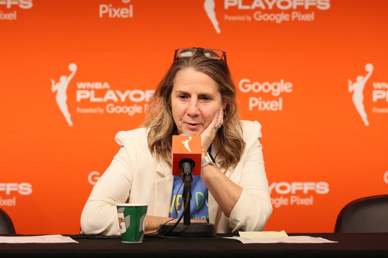 Cheryl Reeve speaks into a microphone in front of a bright orange backdrop