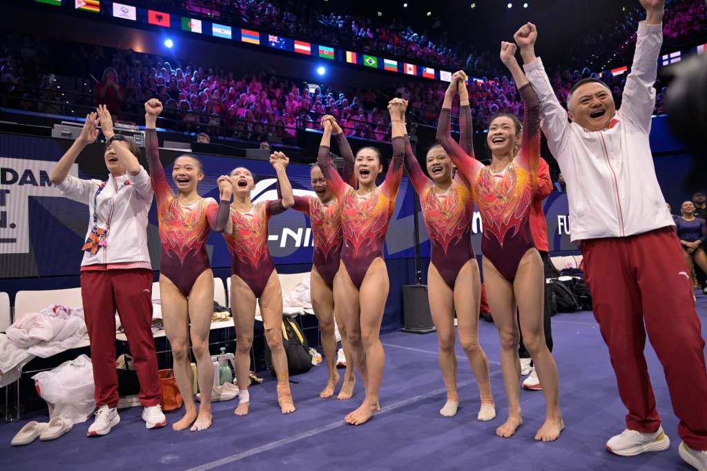 Six gymnasts from Team China celebrate after winning gold at the 2026 world championships.