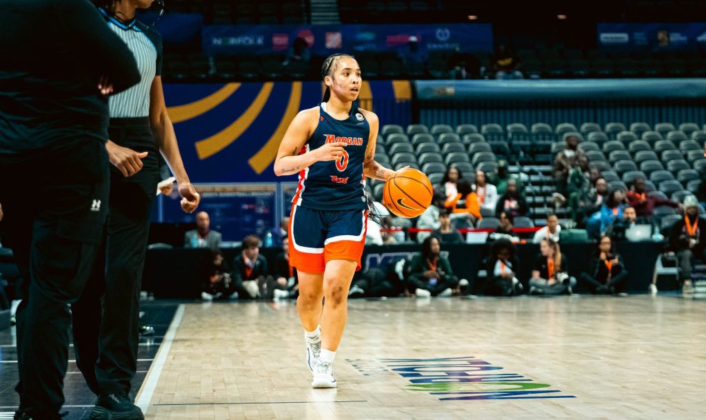 A Morgan State player in a navy blue uniform is dribbling the basketball.