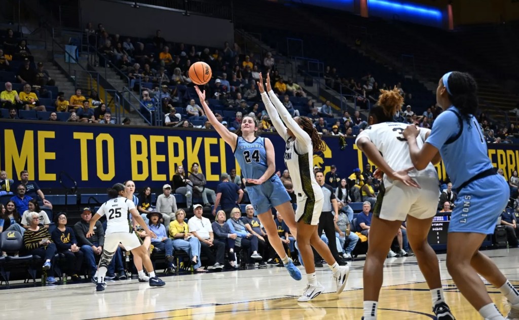 Columbia guard Riley Weiss shoots a right-handed floater. She is leaning to her right, away from a California defender who is contesting the shot with both hands in the air. In the paint, two players jockey for rebounding position as the shot leaves Weissโ hand.