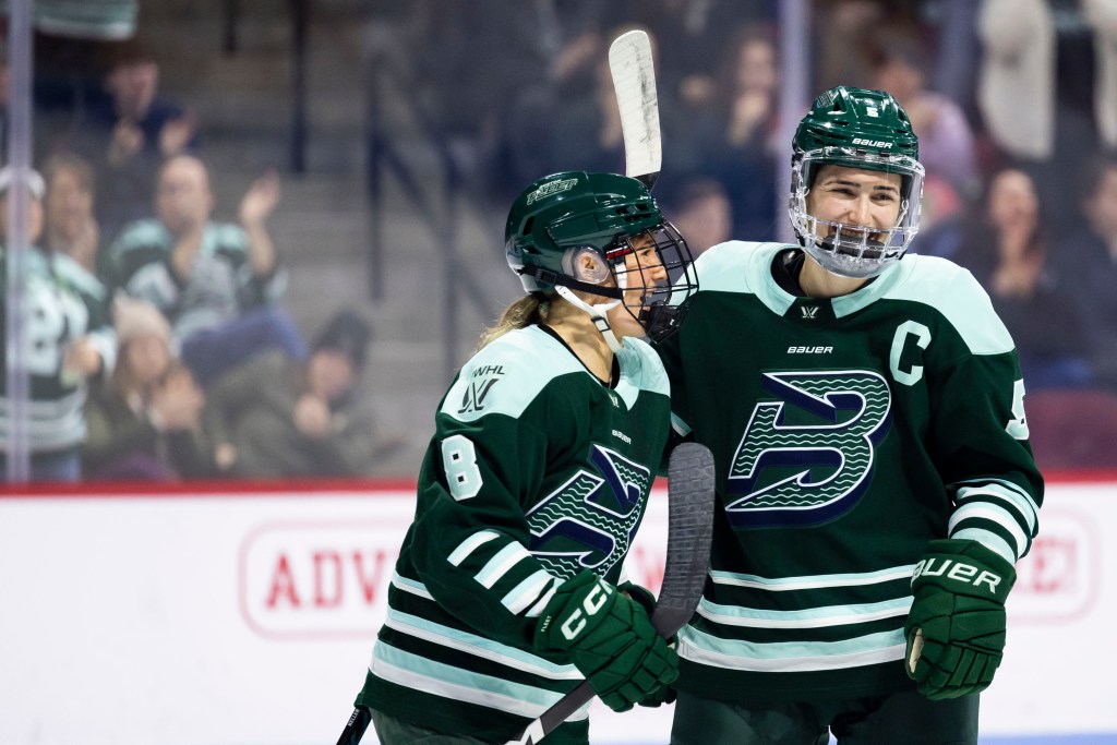 Winn (left) and Keller (right) smile as Winn says something to Keller. They are wearing green home uniforms.