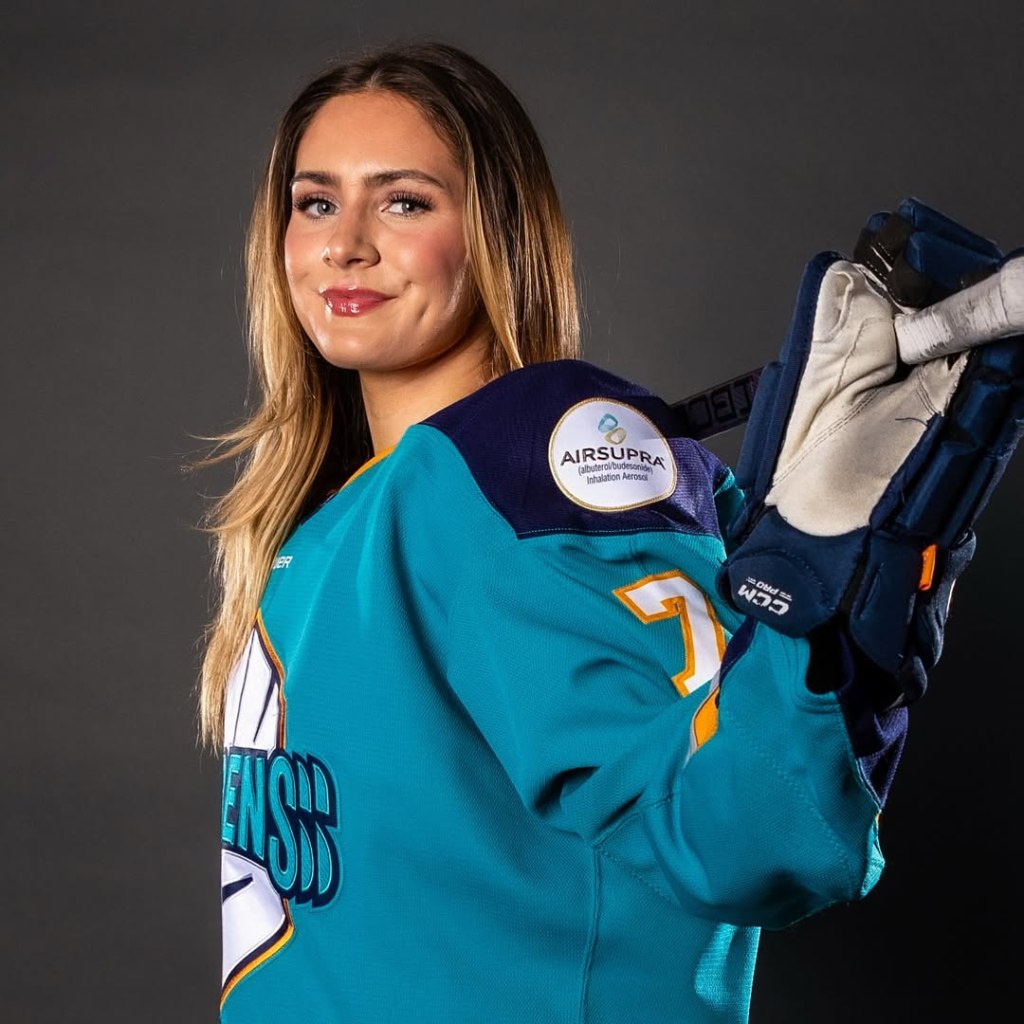 A women's hockey player poses with her hockey stick.