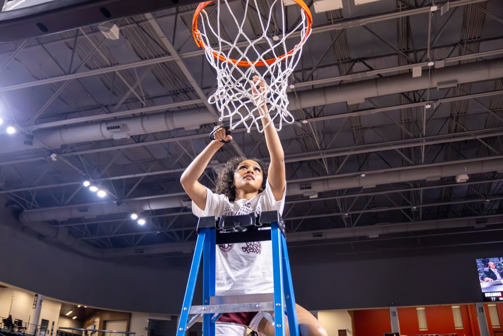 A player climbs a ladder with a pair of scissors and prepares to cut the net.