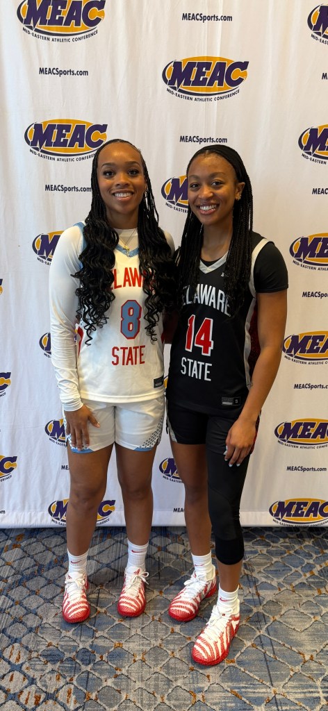 Two players are standing in smiling. The one on the left is in a white uniform and the one on the right is in a black jersey.