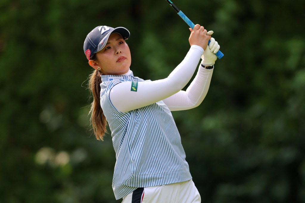 Yuri Yoshida hits a tee shot. Her hands grip the club in the follow-through position as she looks after her shot.