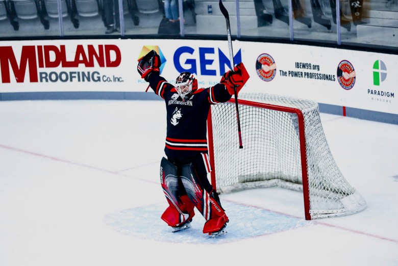 Lisa Jönsson celebrates in the Northeastern goal in her black road jersey with her arms and stick over her head